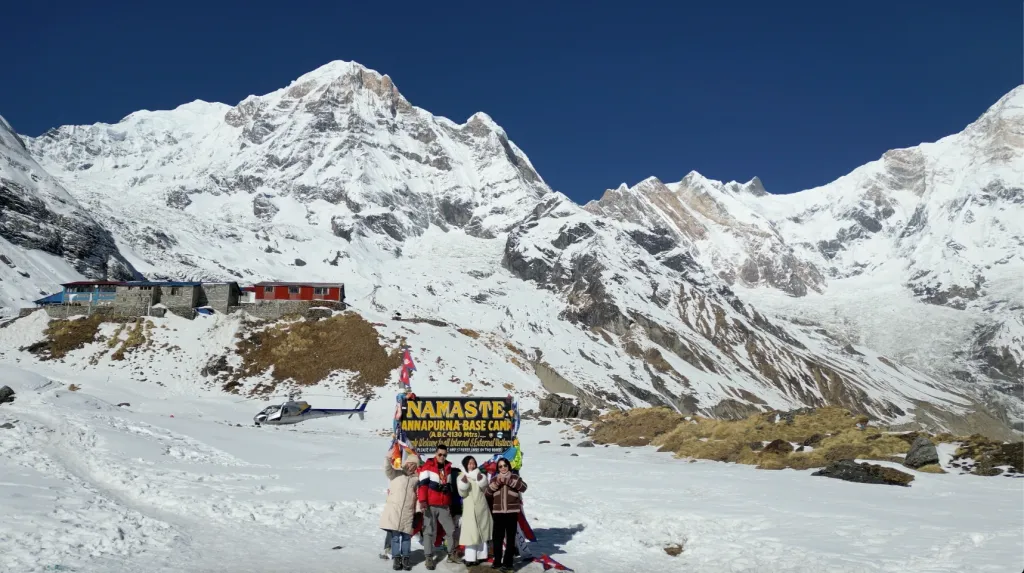 Guest from North Nepal Trek, two men, two women clicking photo infront of Annapurna Base Camp Board, during Annapurna Base Camp Helicopter Tour. 